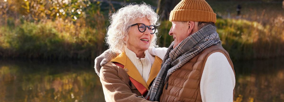 Elderly couple hugging besides the river during autumn