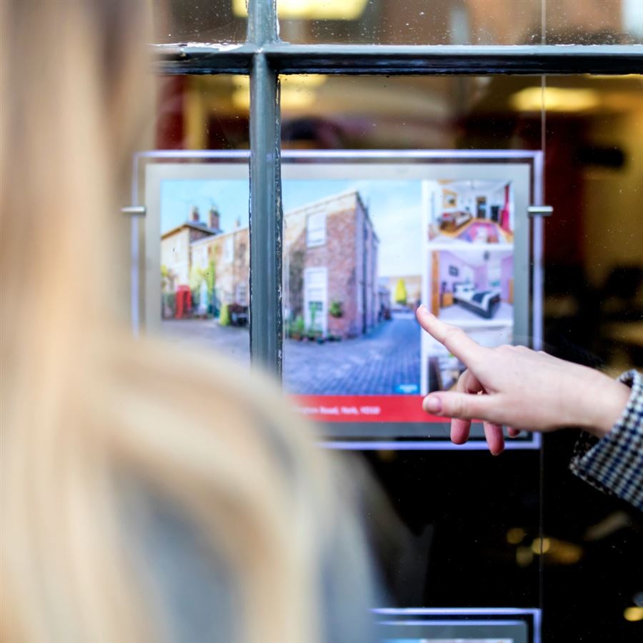 Homebuyers pointing to property listing through estate agent's window