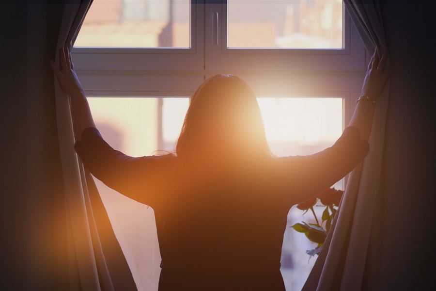 Woman opening curtains to sunshine