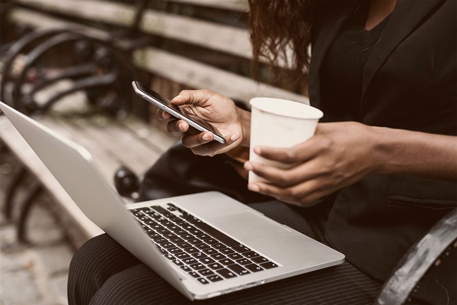 Woman with laptop on her lap, holding a mobile and cup