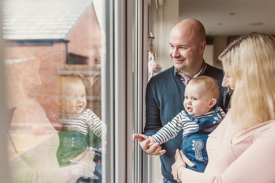 Father, mother and child smiling by window of house