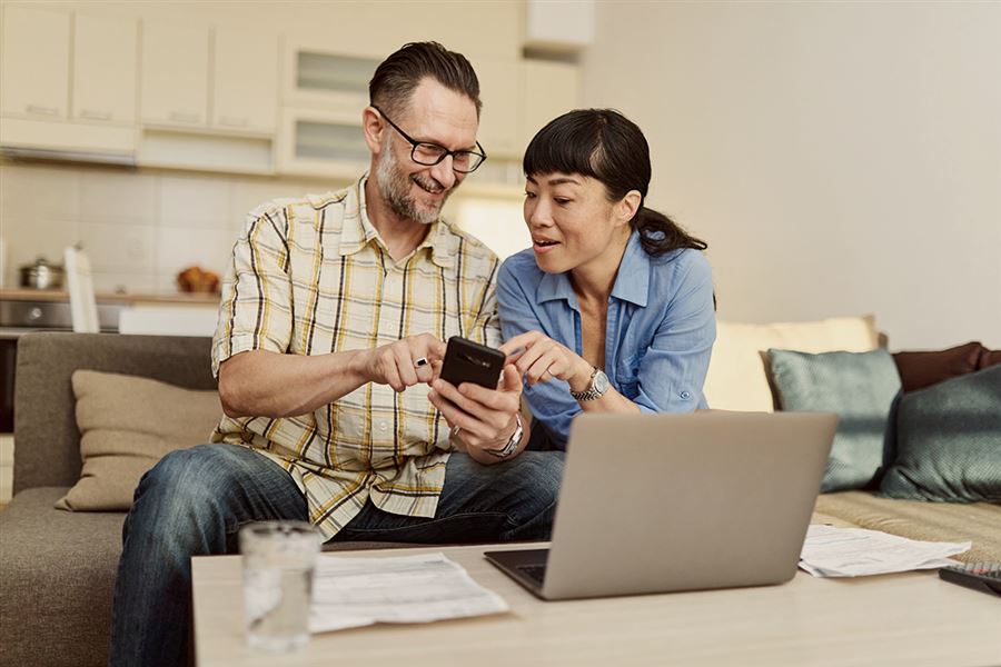 Couple smiling looking at mobile and laptop